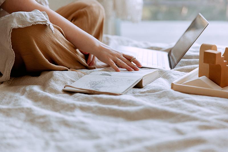 person sitting on bed with computer and book